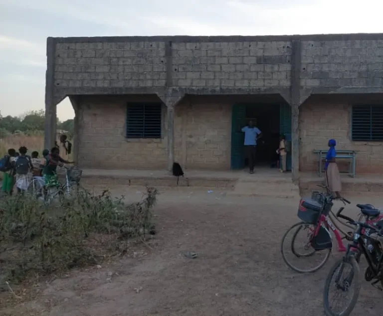 Façade du bâtiment des classes en briques, portes vertes, vélos garés devant.