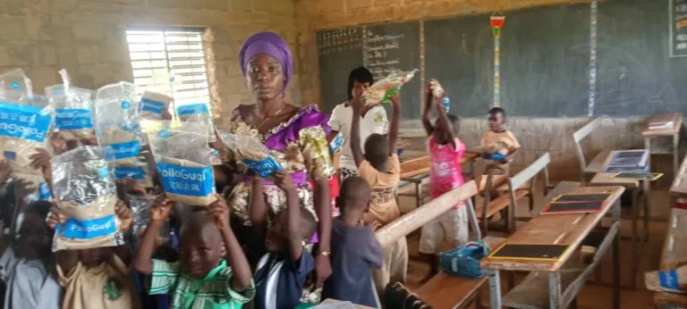 Une classe d’élèves lève ses kits au-dessus des têtes, entre les tables-bancs.